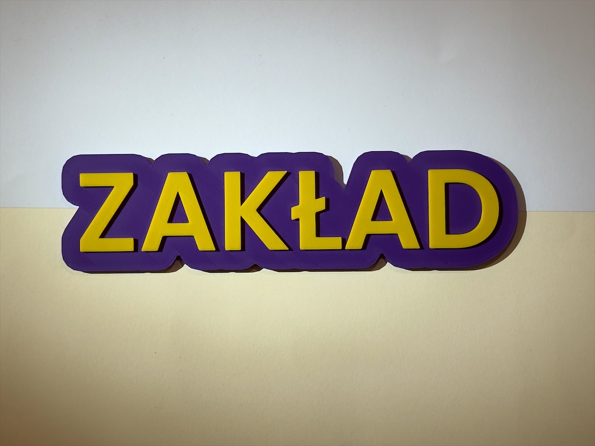 The Napis - napis na drzwi ZAKŁAD, fioletowa baza i żółte litery, na jasnym dwubarwnym tle